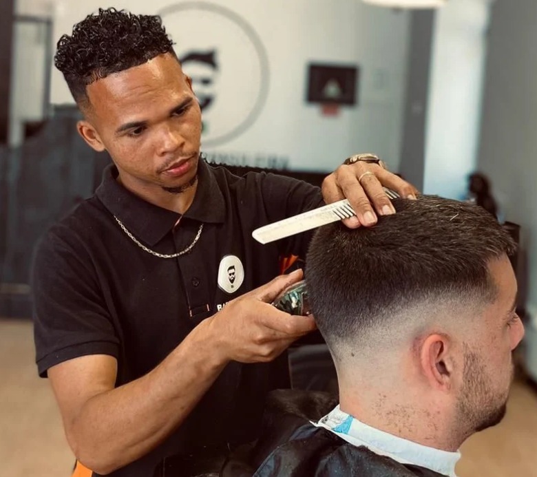 Barbeiro finalizando um degradê com pente e máquina